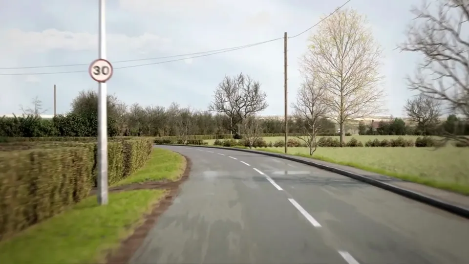 A rural road winds through open arable fields with hedgerows, telegraph poles and a red-brick farmhouse.
