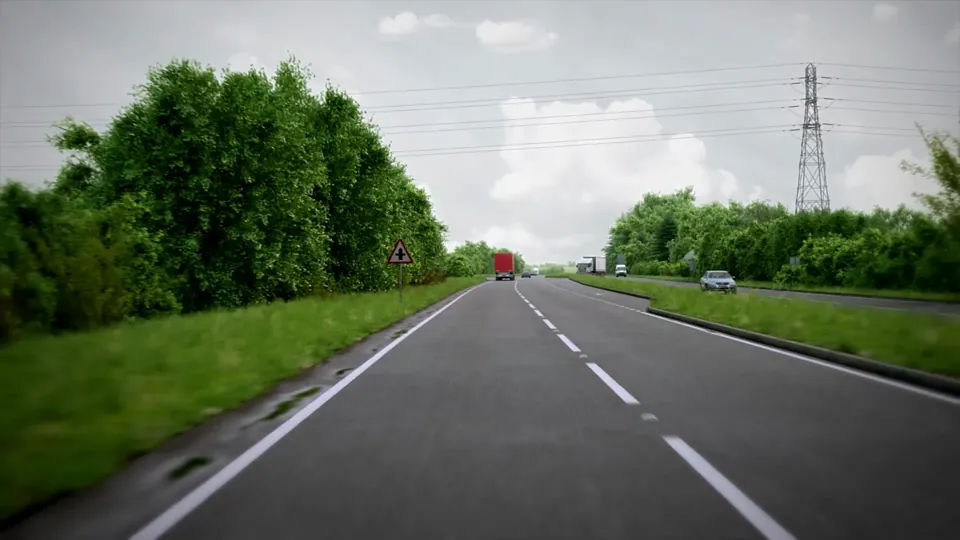 A dual carriageway cuts through green countryside with a central crash barrier, hedgerows, lighting columns and a roadside petrol station.