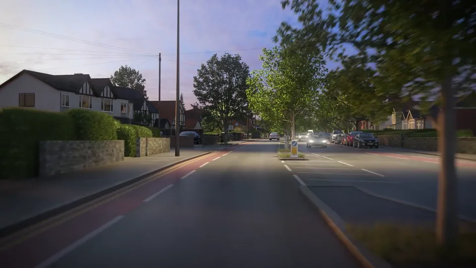 A suburban avenue at dusk with red cycle lanes, a tree-planted refuge island and half-timbered houses, street lamps lit and headlights approaching under a violet sky.