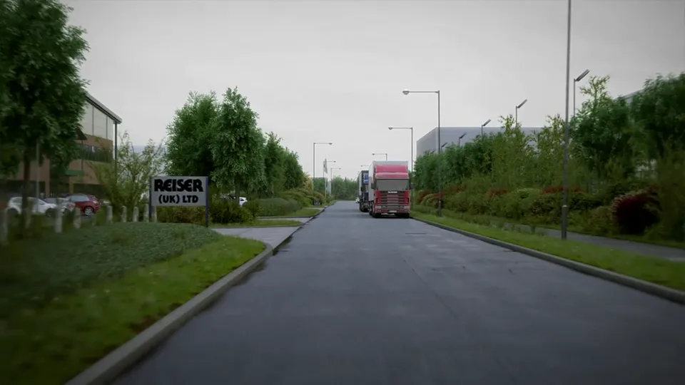 A wide industrial-estate road with landscaped verges and young trees, articulated lorries parked along the kerb and a company nameboard at an entrance.