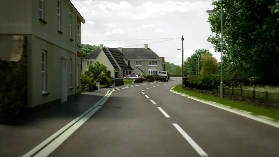 A rural road descends into a village through dense green foliage and stone walls, with hills rising behind.
