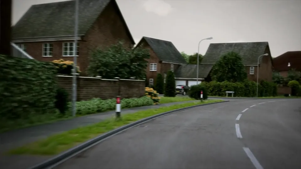 A winding suburban estate road lined with detached red-brick houses, trimmed hedges and regular streetlamps.