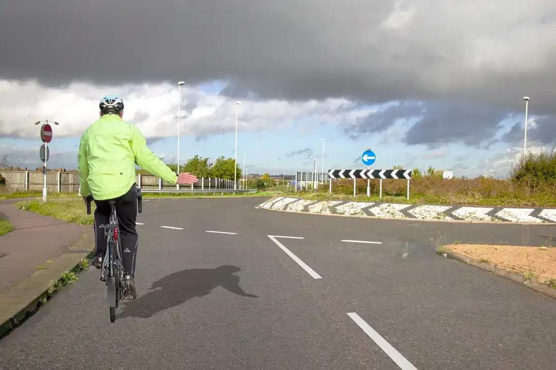Illustration for the question: You're approaching this roundabout. What should you do when a cyclist is keeping to the left while signalling to turn right?