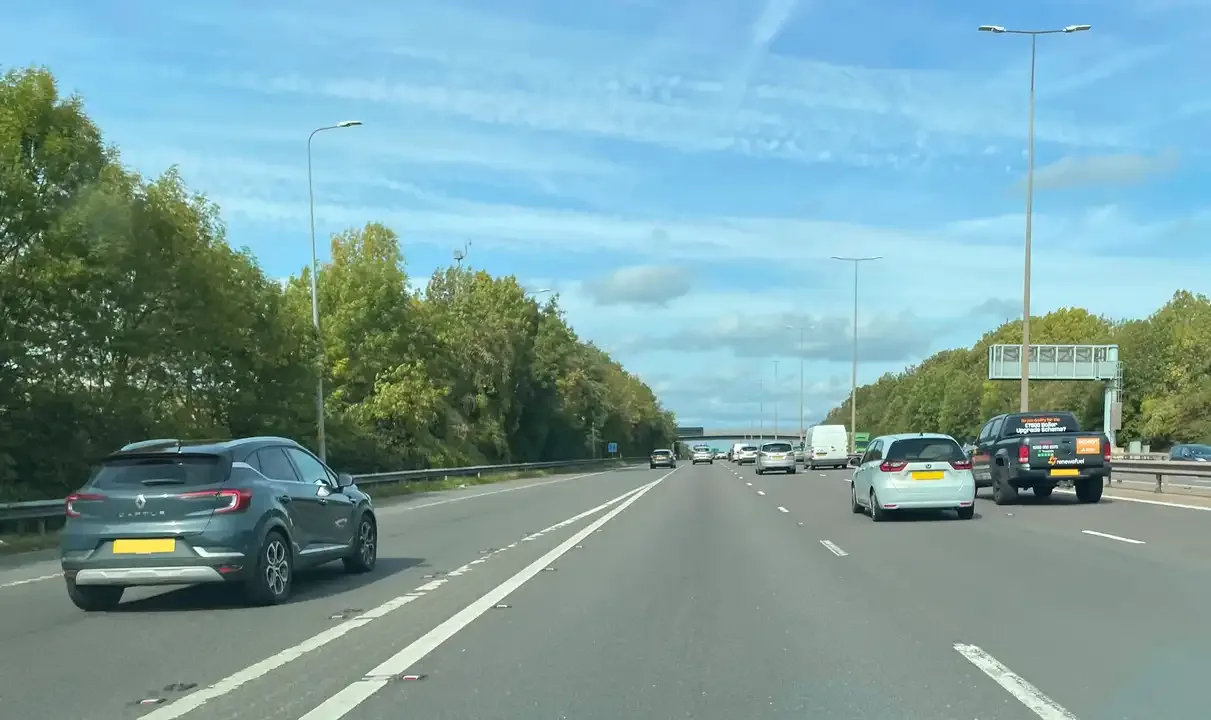 Illustration for the question: Your pupil is driving along the left-hand lane of a three-lane motorway. You see traffic is joining from a slip road ahead. What should you suggest your pupil does to help maintain the traffic flow?